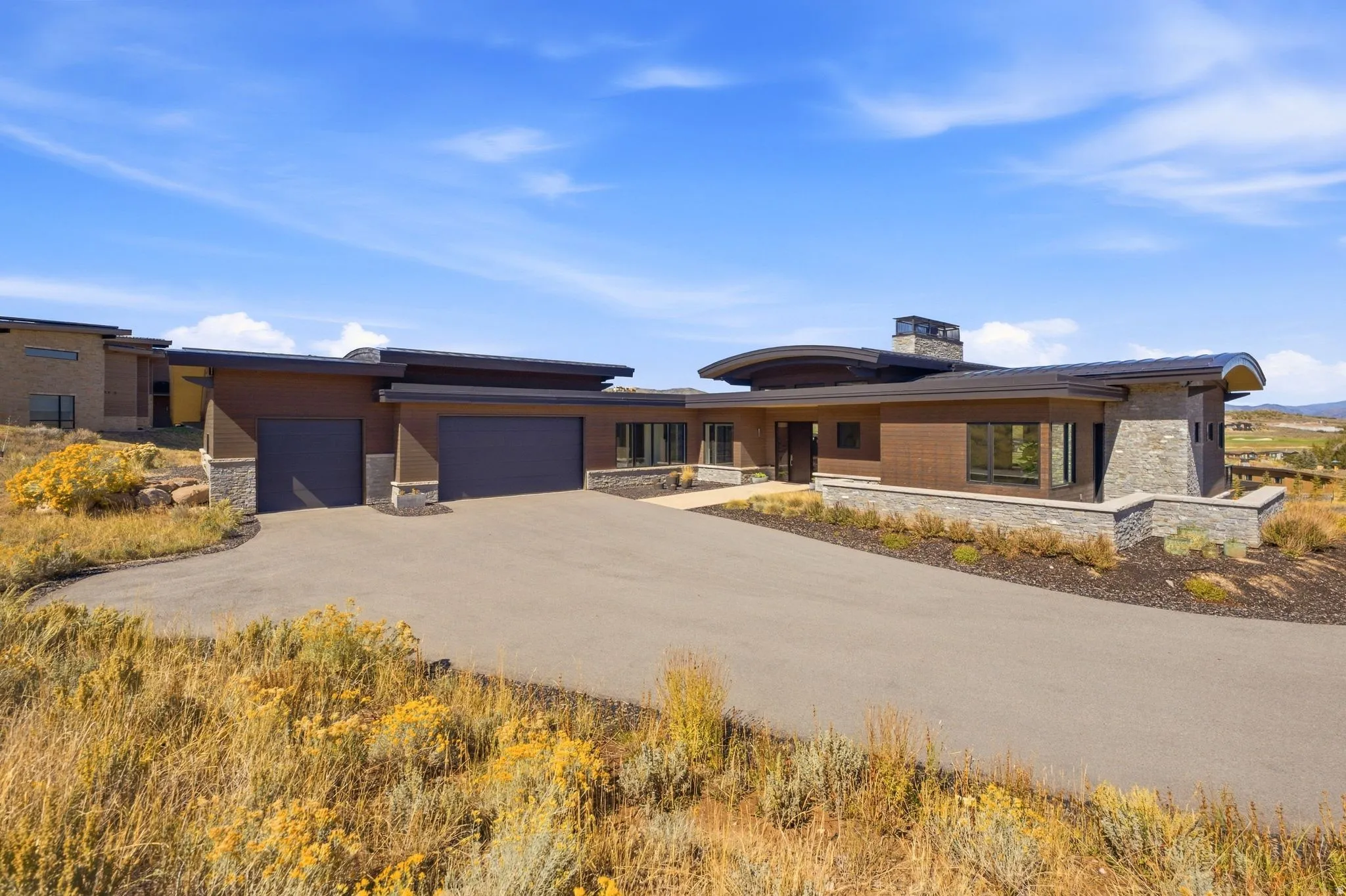 Contemporary architecture featuring a two-car garage, stone and wood-finish exterior, and an expansive paved driveway