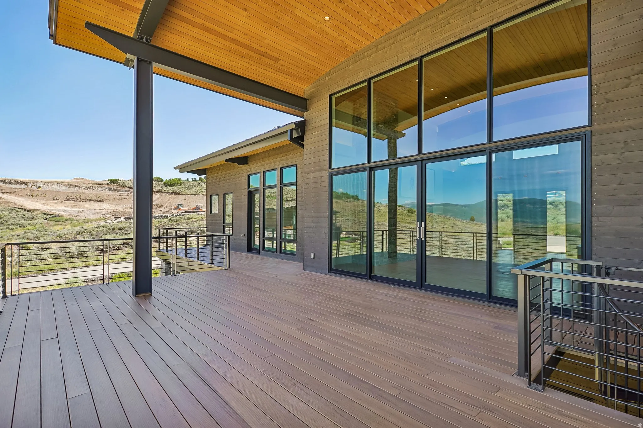 Expansive outdoor deck featuring wood-finish flooring, a wood-paneled ceiling, and black metal railings