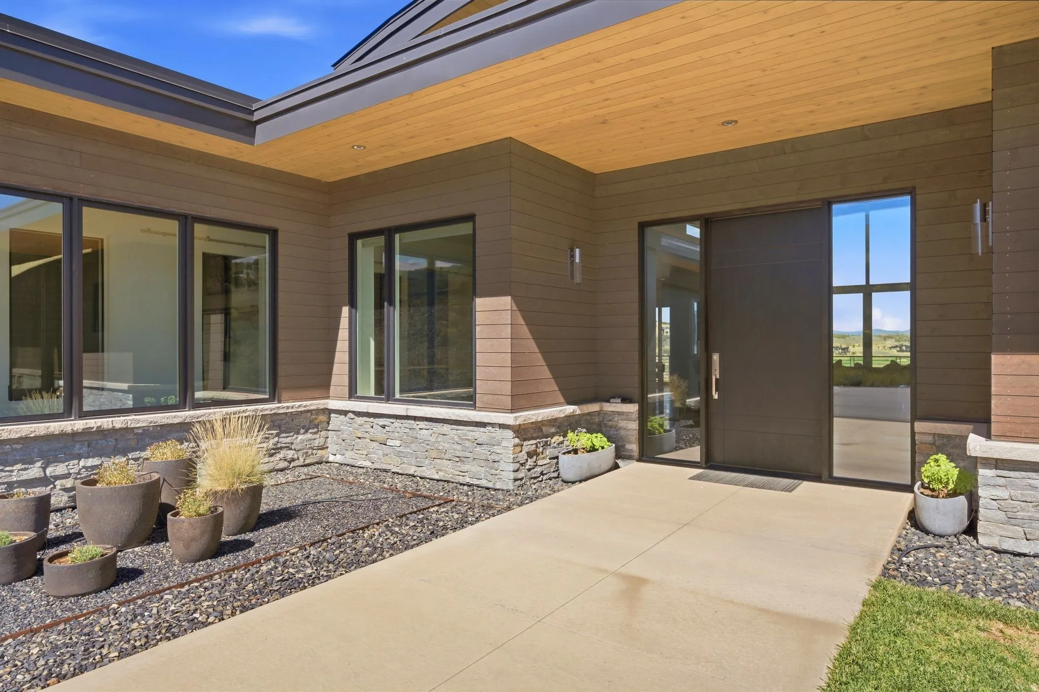 Modern exterior with wood-finish soffit, stone veneer detailing, and large dark-framed windows