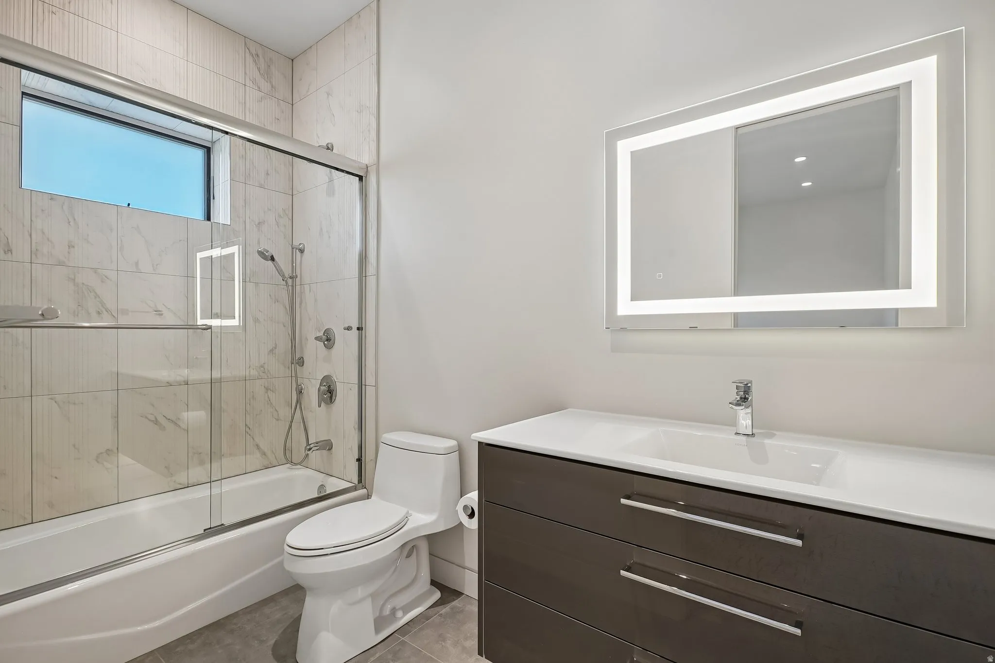 Bathroom featuring a single vanity with integrated sink, dark wood-finish cabinetry, and an illuminated mirror