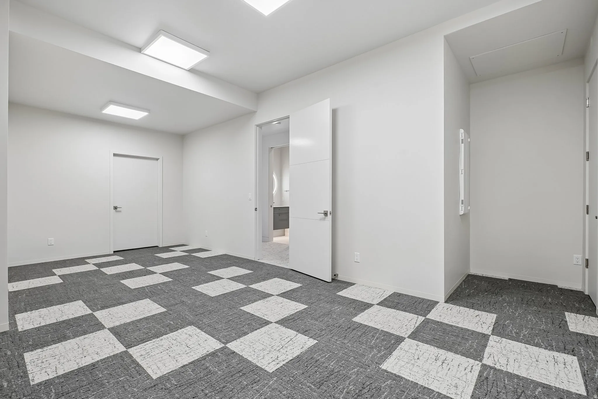 Spacious room featuring geometric pattern carpeting, contemporary white walls, modern flush-mount lighting, and white interior doors