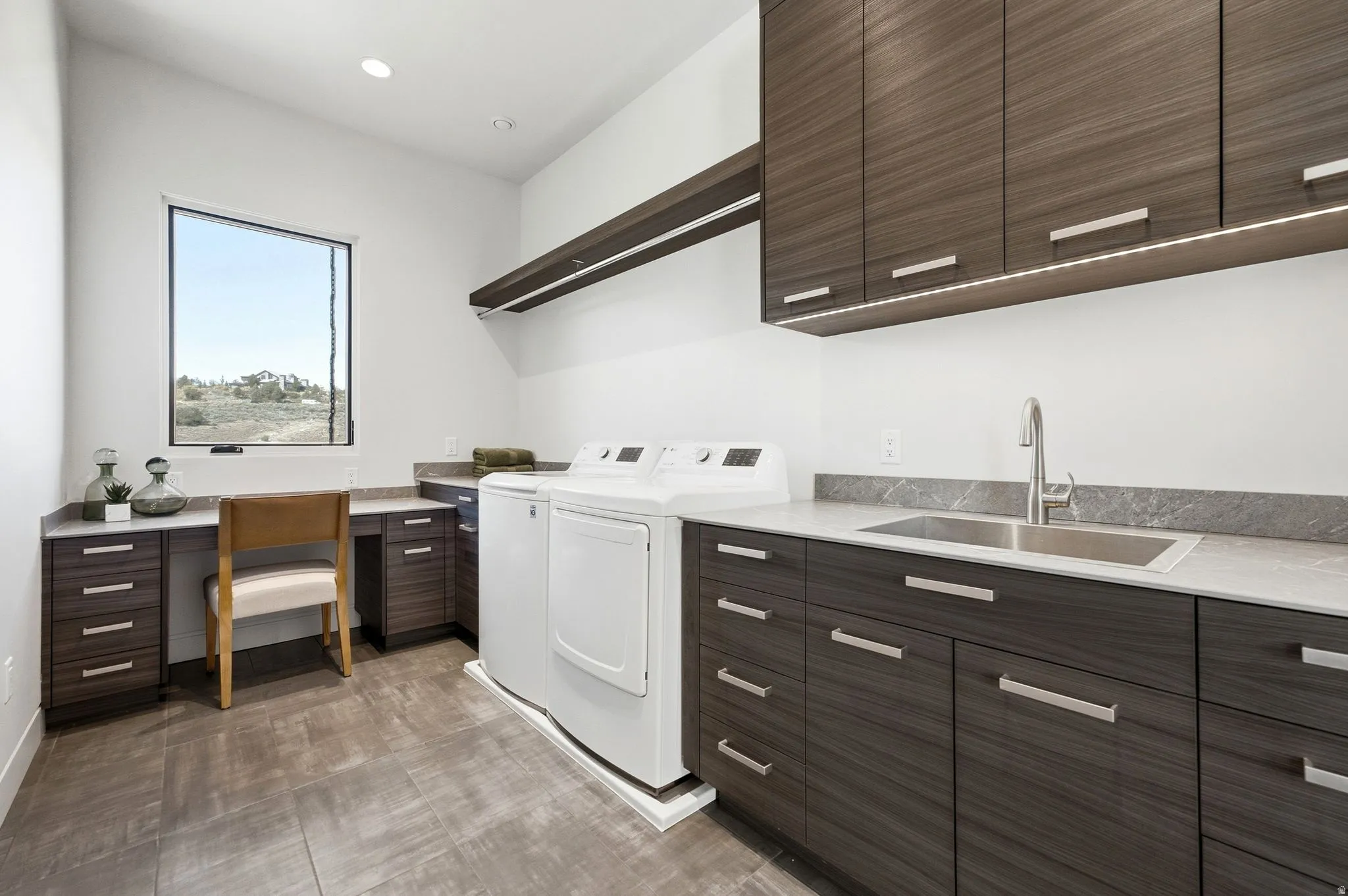 Integrated utility room with ample dark wood-finish cabinetry, a built-in stainless steel sink, and a dedicated workspace
