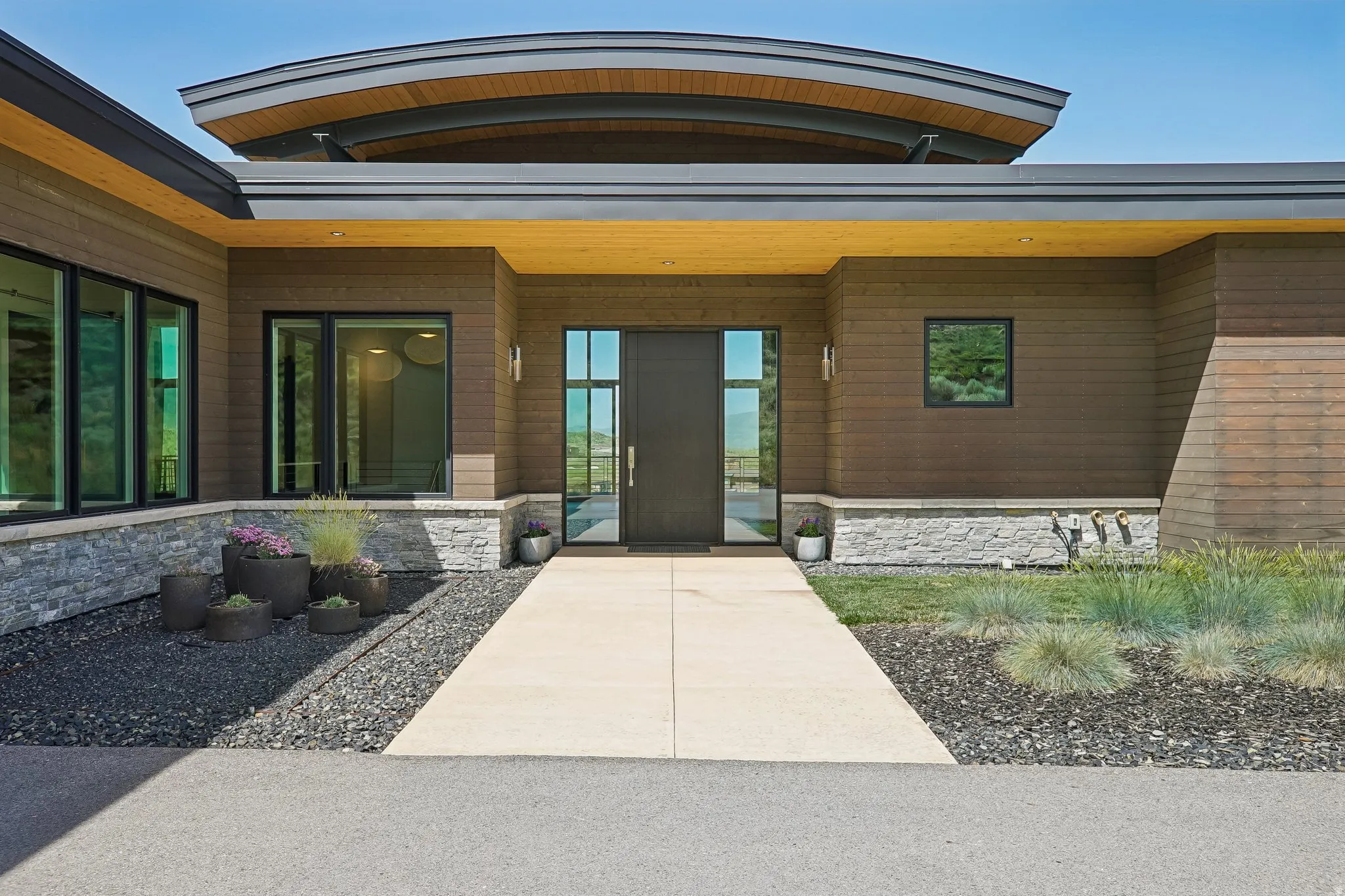Contemporary exterior featuring wood-finish siding, stone accents, a concrete walkway, and a dark entry door with vertical windows