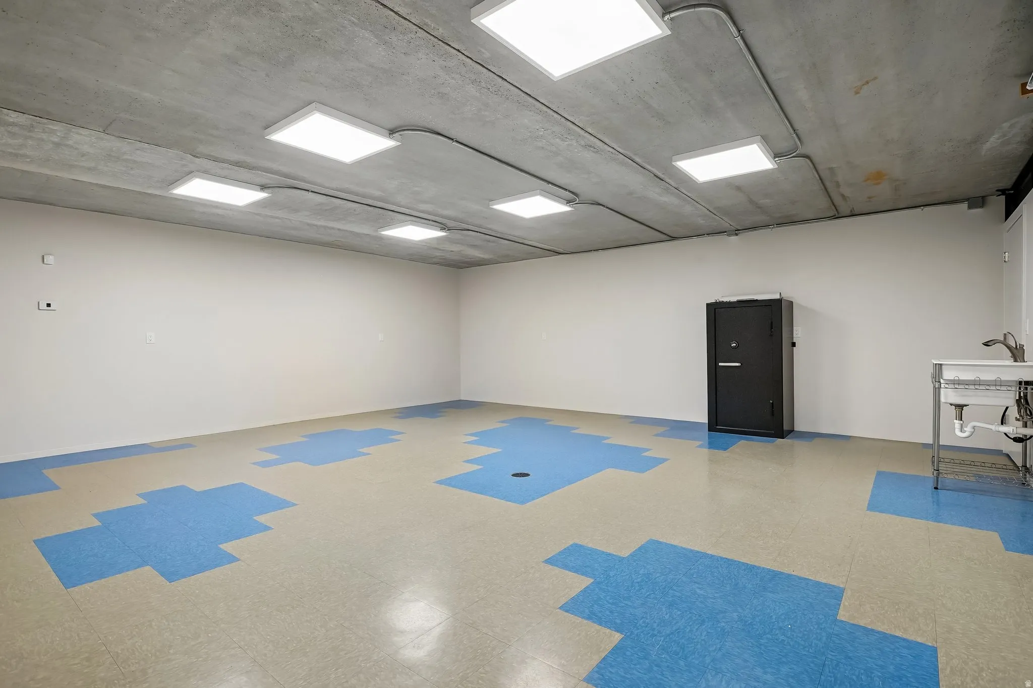 Spacious room featuring a concrete ceiling with multiple recessed square light fixtures, neutral walls, and a multi-toned blue and tan patterned floor
