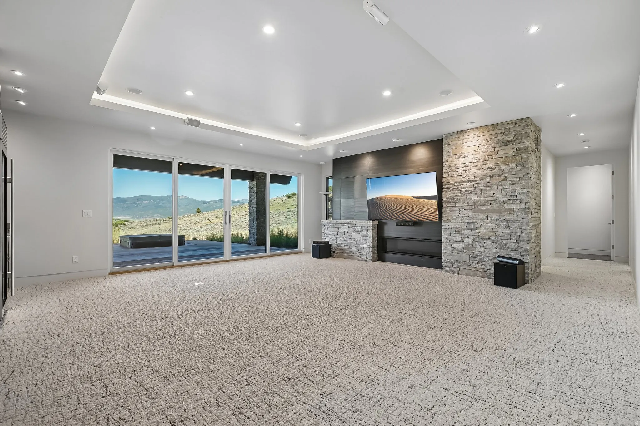 Spacious room featuring broad sliding glass doors, a stone veneer accent wall, recessed lighting, a tray ceiling with integrated lighting, and carpeted flooring