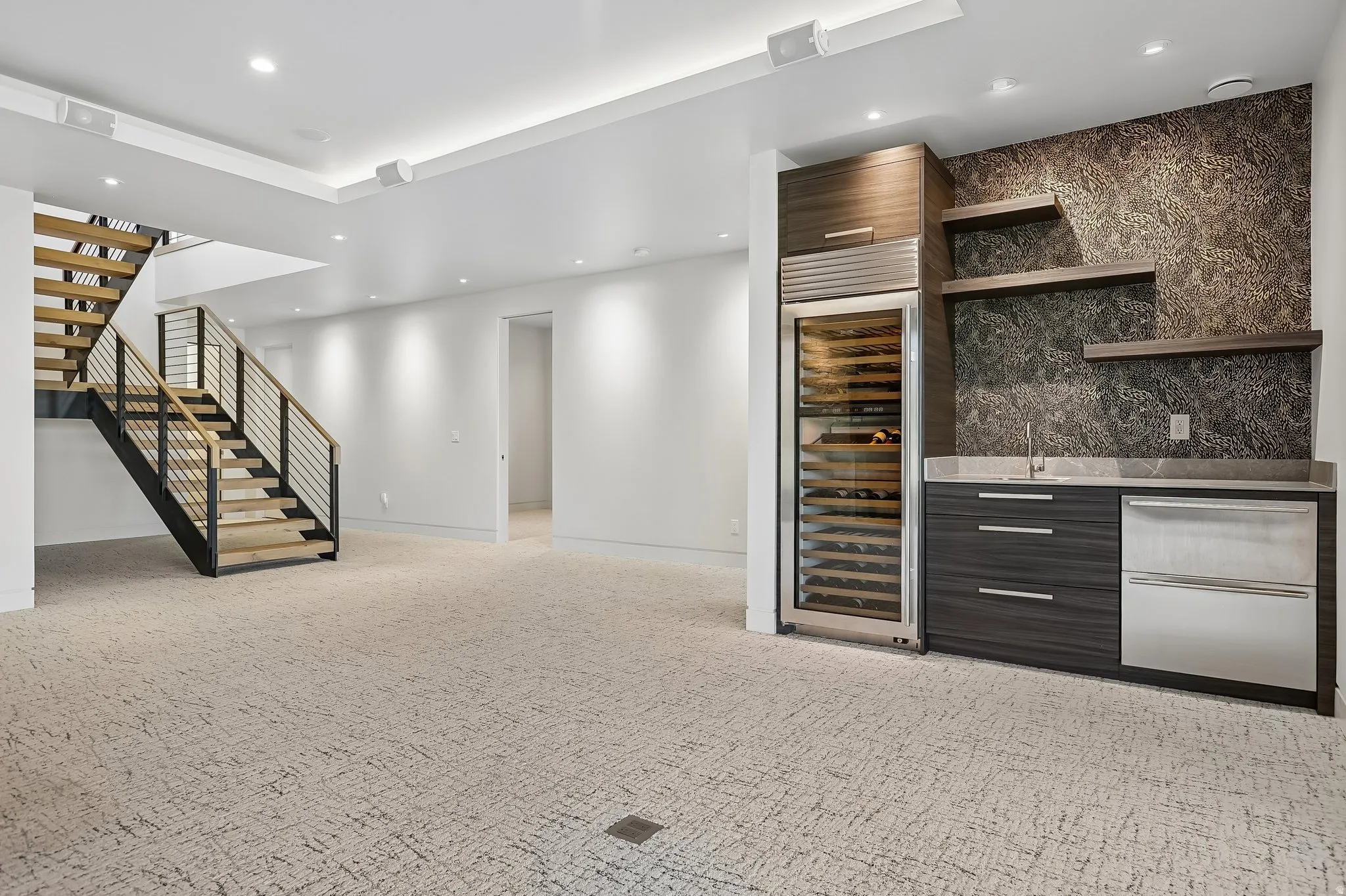 Spacious lower-level area featuring a modern staircase with wood treads and metal railing, recessed lighting, and patterned carpet flooring