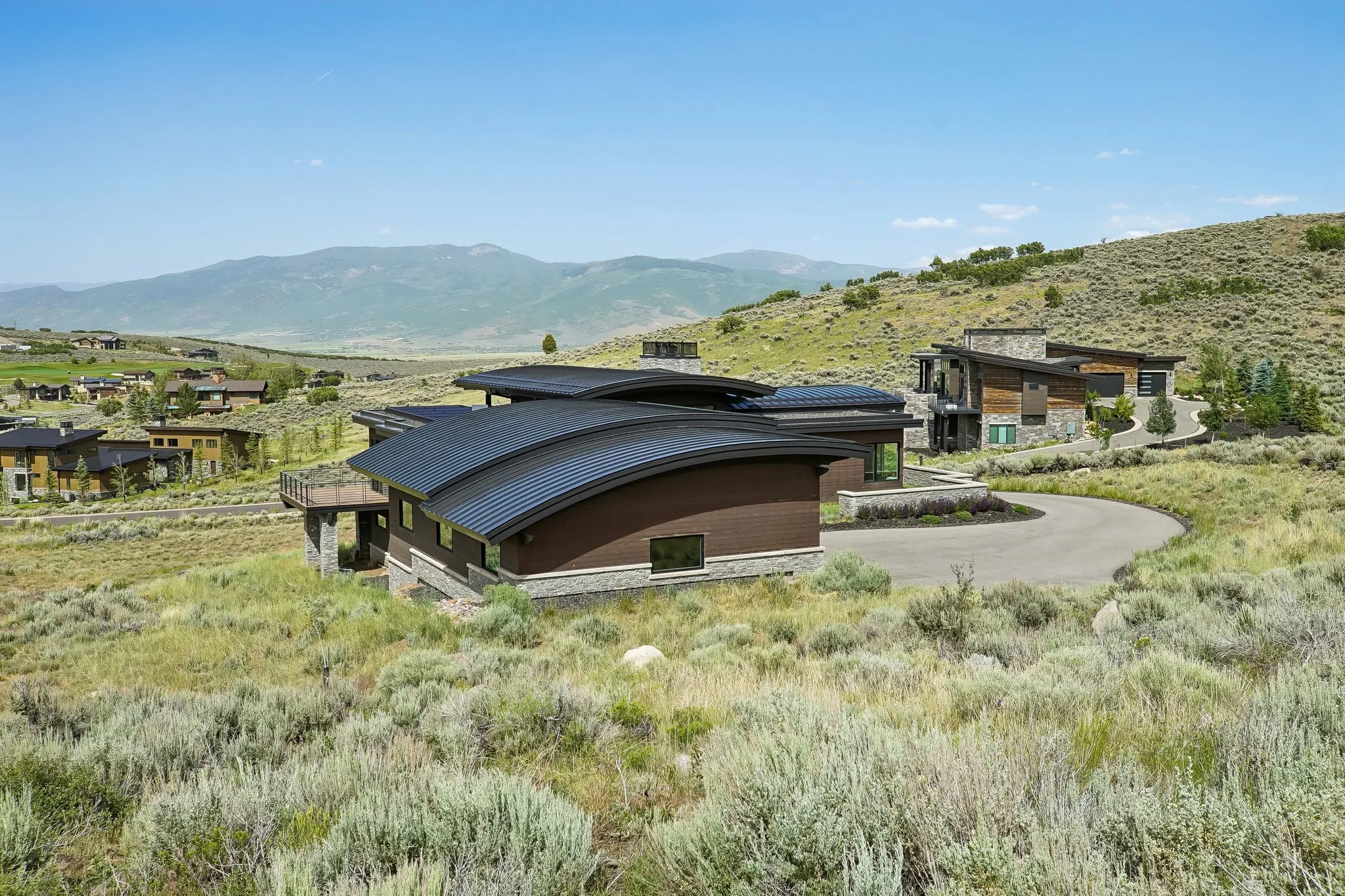 Contemporary mountain home featuring a curved metal roof, stone foundation, and natural wood siding