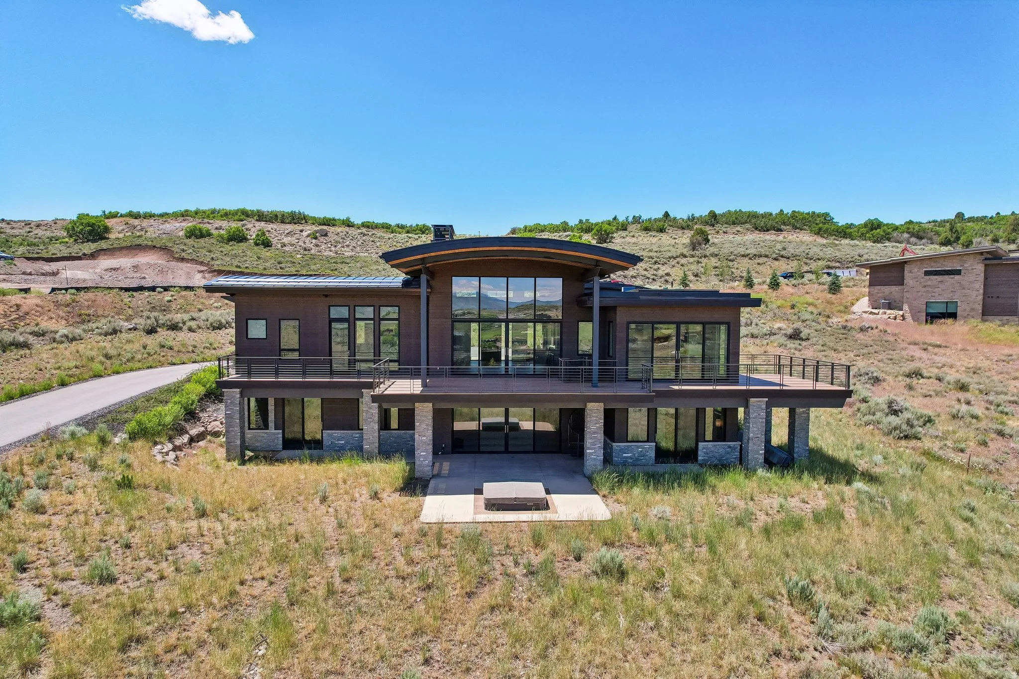 Contemporary architecture featuring expansive glazing, a curved roofline, and a prominent upper-level deck