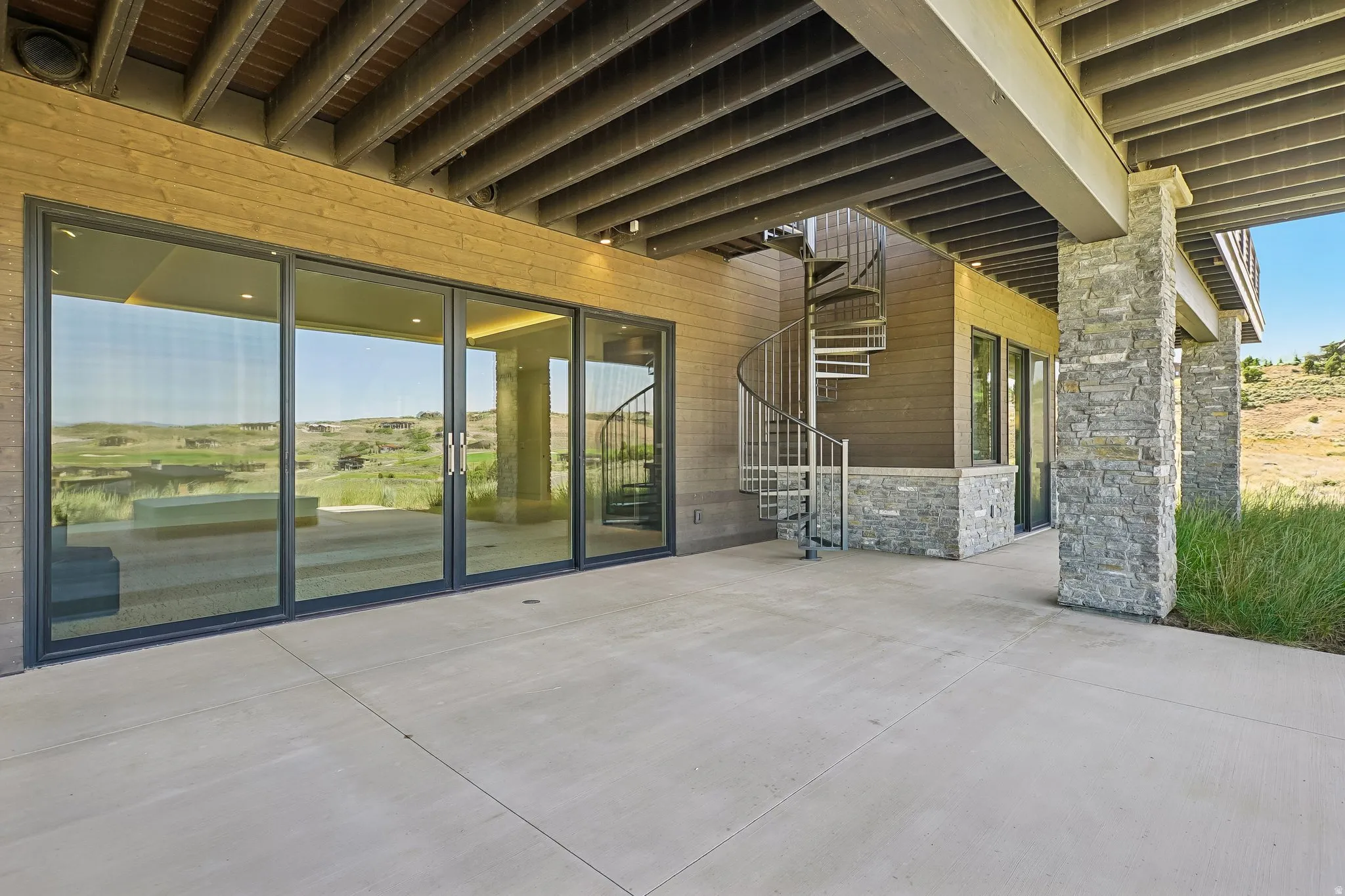 Concrete patio with a spiral staircase, stone veneer columns, wood-finish siding, and large glass sliding doors