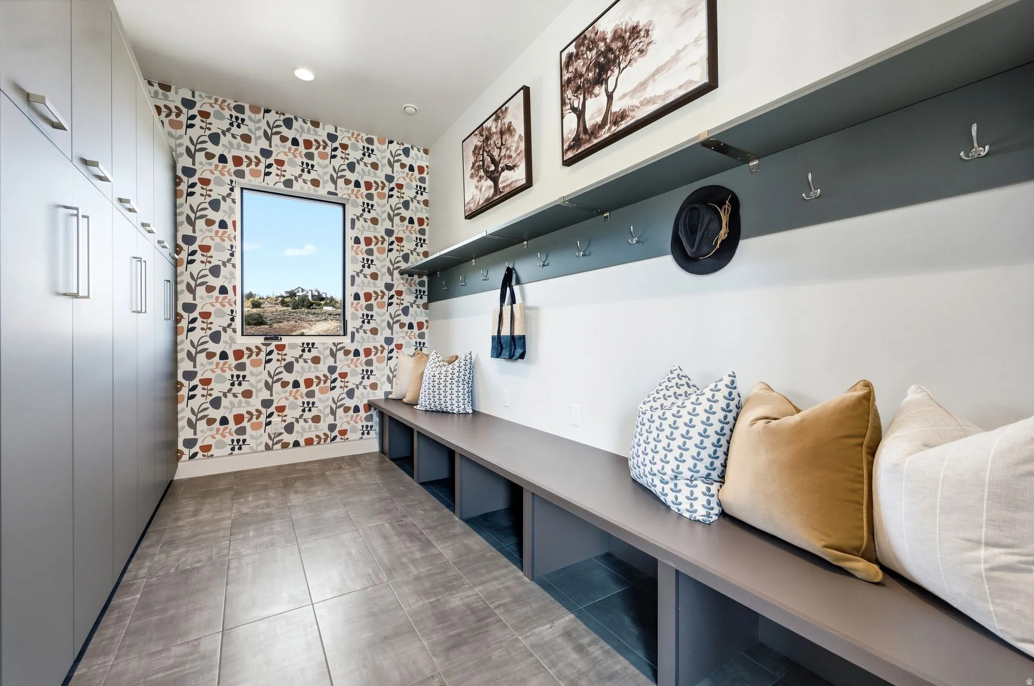 Built-in storage cabinetry, tiled flooring, built-in bench seating with cubbies, accent wall, and a horizontal window