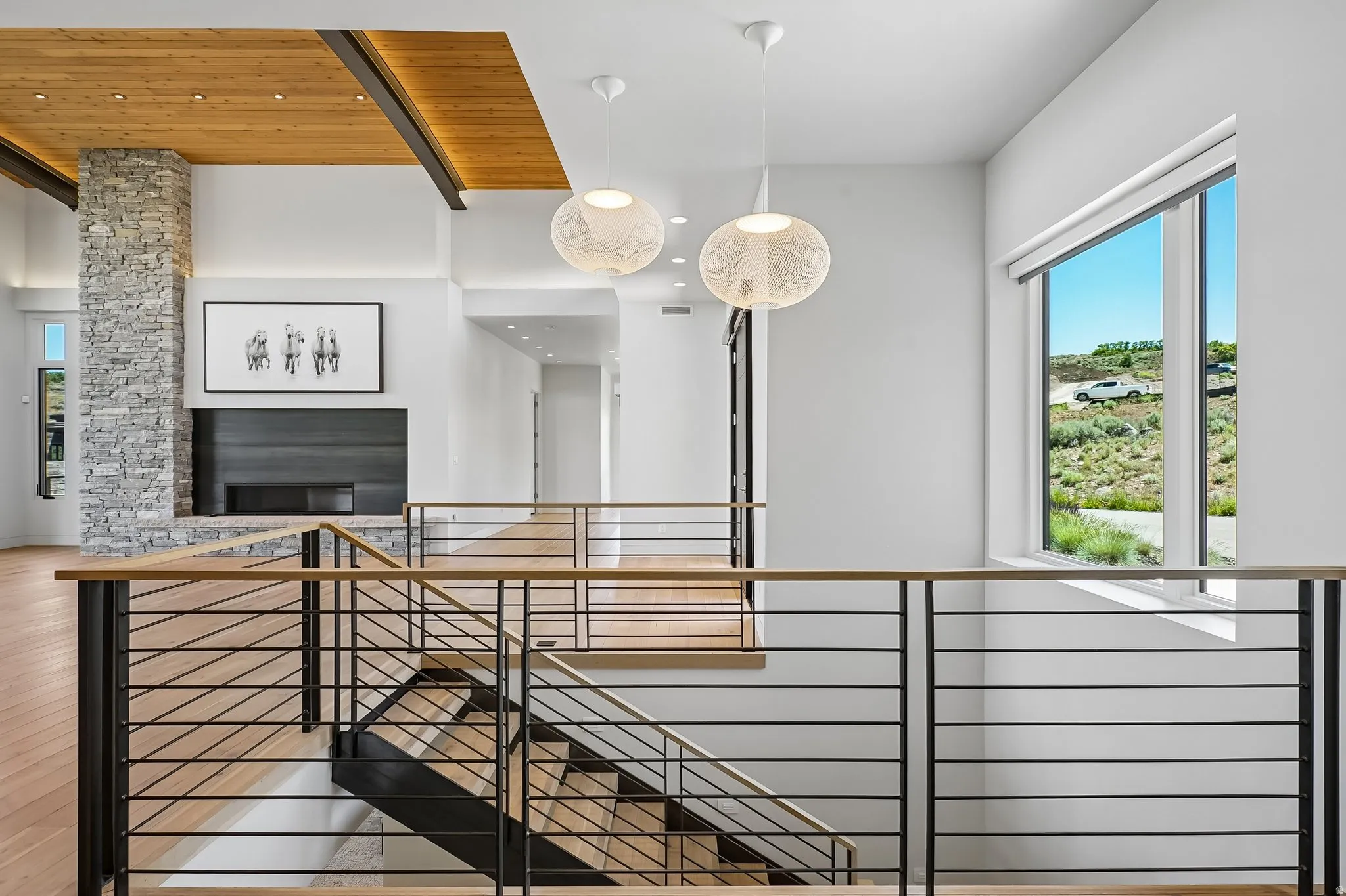 Multi-level interior featuring a stone-clad fireplace and hearth, wood-finish flooring, and a modern staircase with wood handrails and black metal balusters