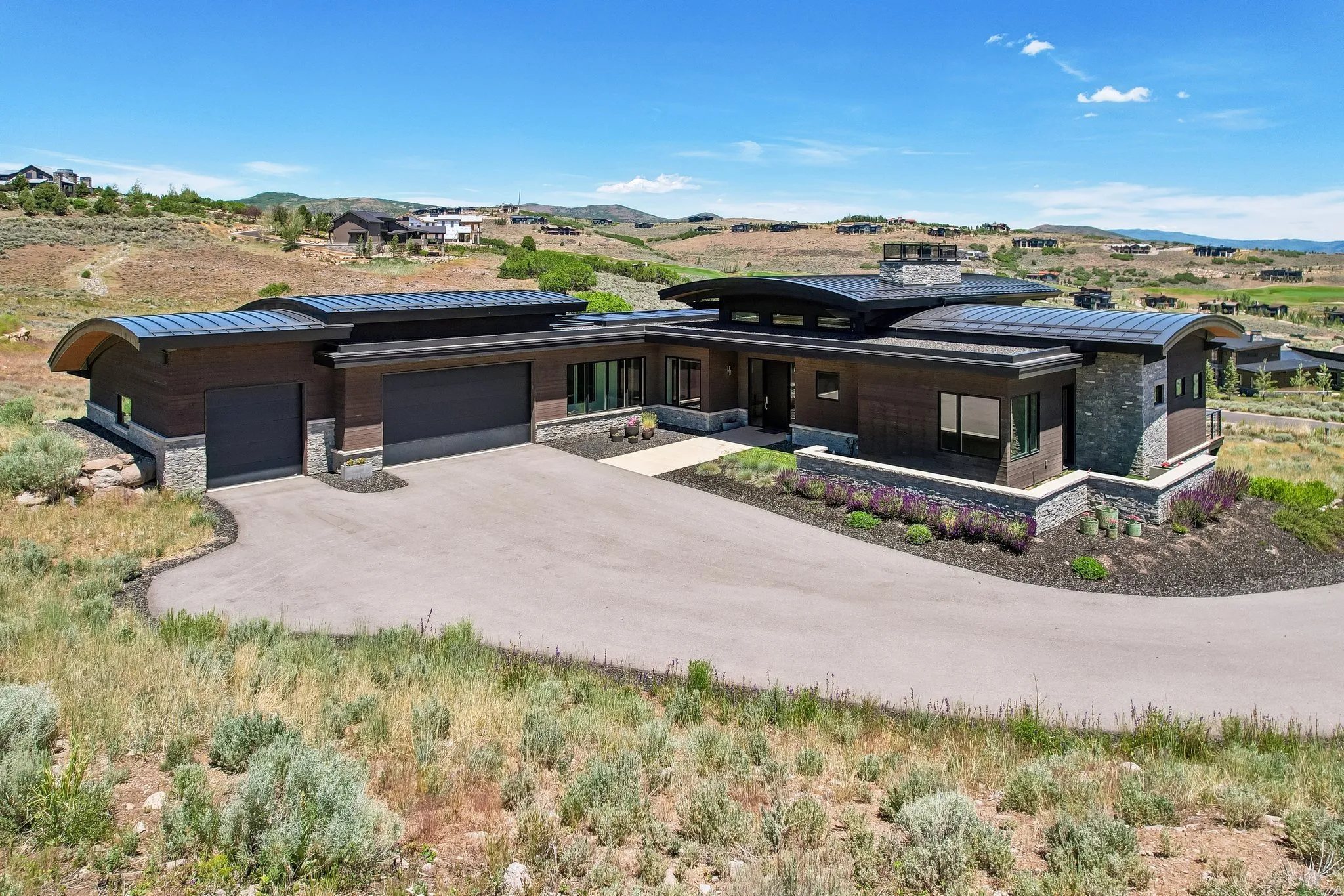 Contemporary architectural design featuring a curved metal roof, stone veneer accents, and a multi-car garage with dark doors