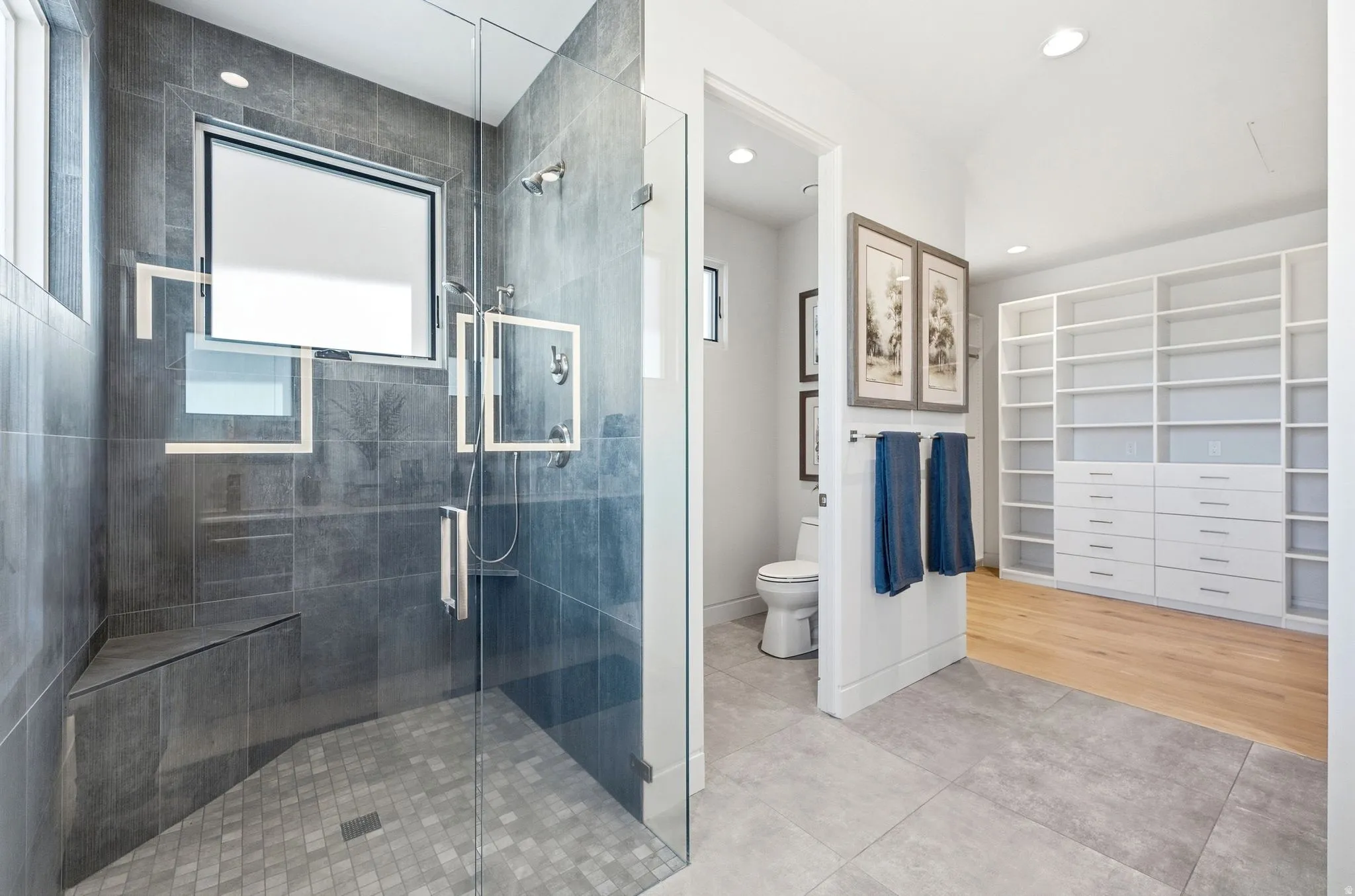 Glass-enclosed shower with dark gray tile, built-in bench, and dual shower heads