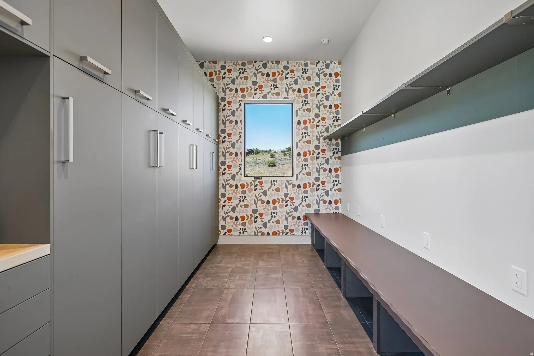 Spacious room featuring extensive built-in cabinetry with contemporary hardware, wood-finish flooring, a patterned accent wall, and a long built-in bench with open storage below