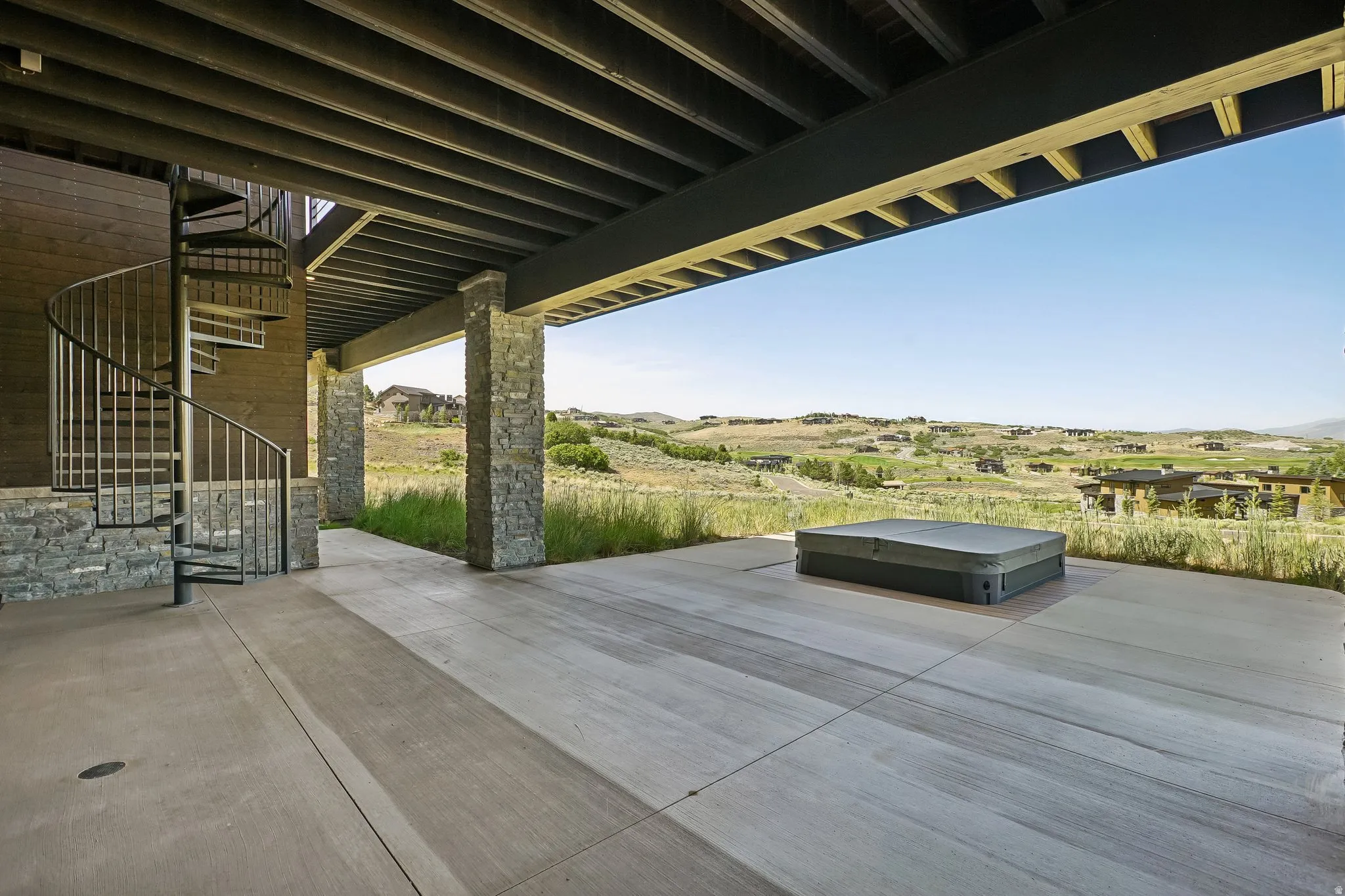Expansive outdoor patio featuring a spiral staircase, stone-clad pillars, and a built-in hot tub