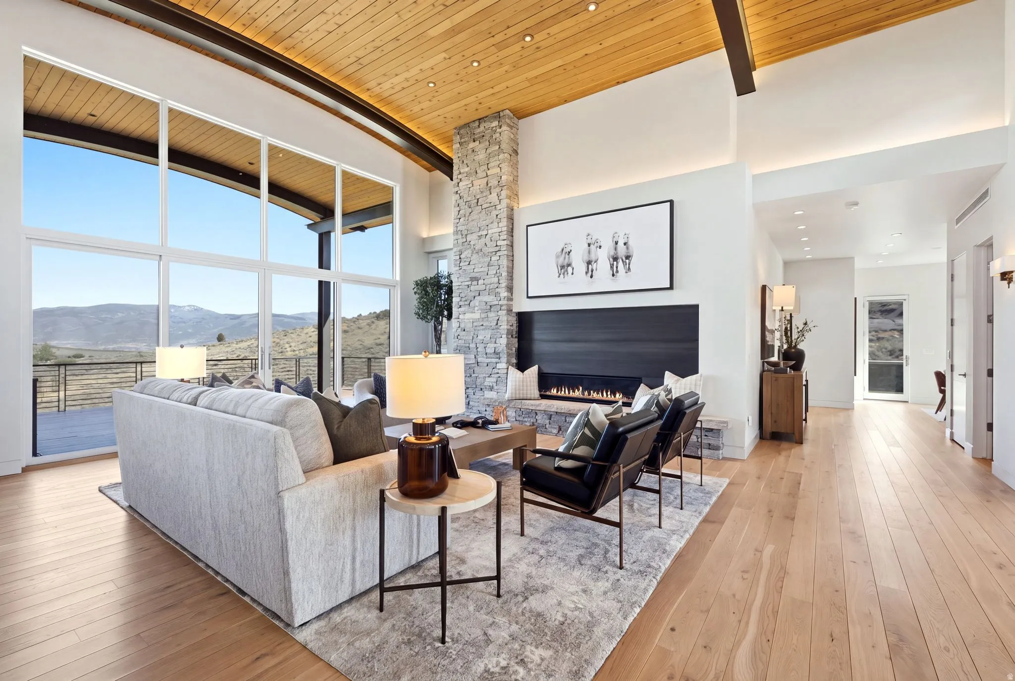 Expansive window wall, wood-finish flooring, stone-clad fireplace, linear gas fireplace, and wood-paneled ceiling