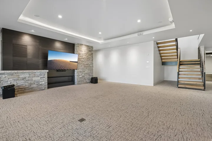 Spacious entertainment area featuring a contemporary fireplace with stone surround, accent wall, recessed lighting, and a floating staircase with wood treads and metal railings