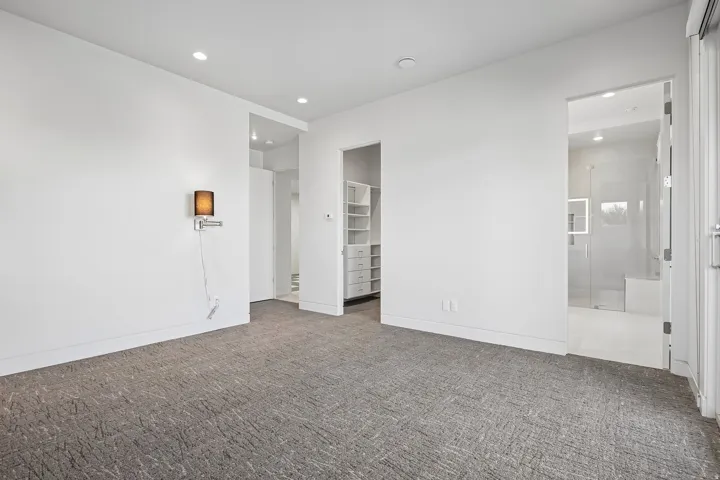 Spacious room featuring textured gray carpeting, crisp white walls, recessed lighting, and a built-in closet system