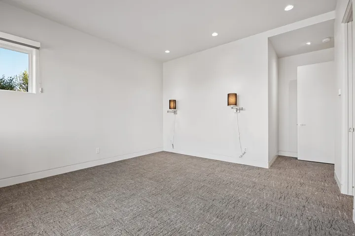 Bright room featuring recessed lighting, a modern window, two wall-mounted sconces, and neutral-toned patterned carpeting