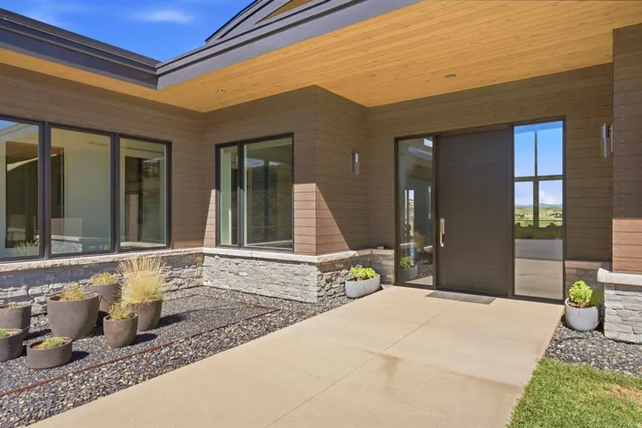 Modern exterior with wood-finish soffit, stone veneer detailing, and large dark-framed windows