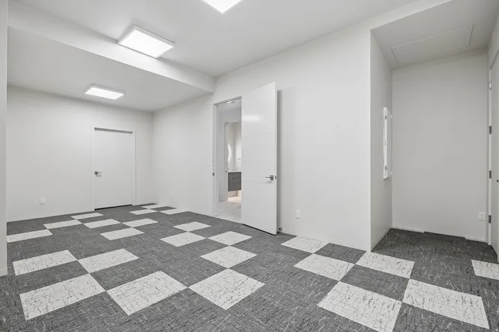 Spacious room featuring geometric pattern carpeting, contemporary white walls, modern flush-mount lighting, and white interior doors
