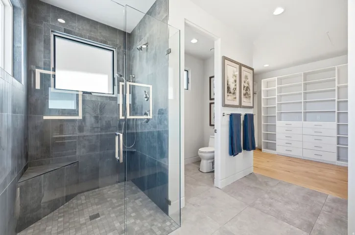 Glass-enclosed shower with dark gray tile, built-in bench, and dual shower heads