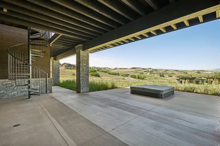 Expansive outdoor patio featuring a spiral staircase, stone-clad pillars, and a built-in hot tub