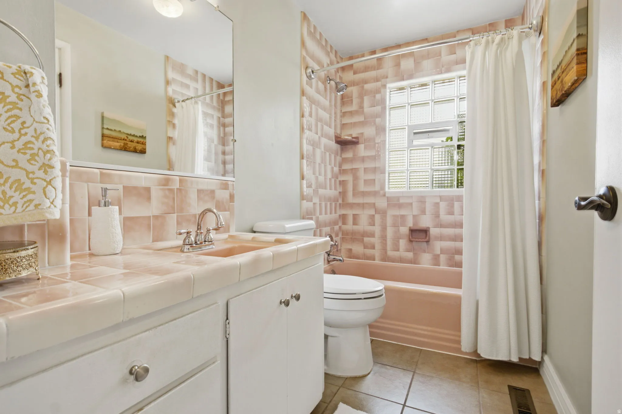 Bathroom featuring a tiled vanity with integrated sink, white cabinetry with silver-tone hardware, and a tub-shower combination with patterned wall tiling and glass block window