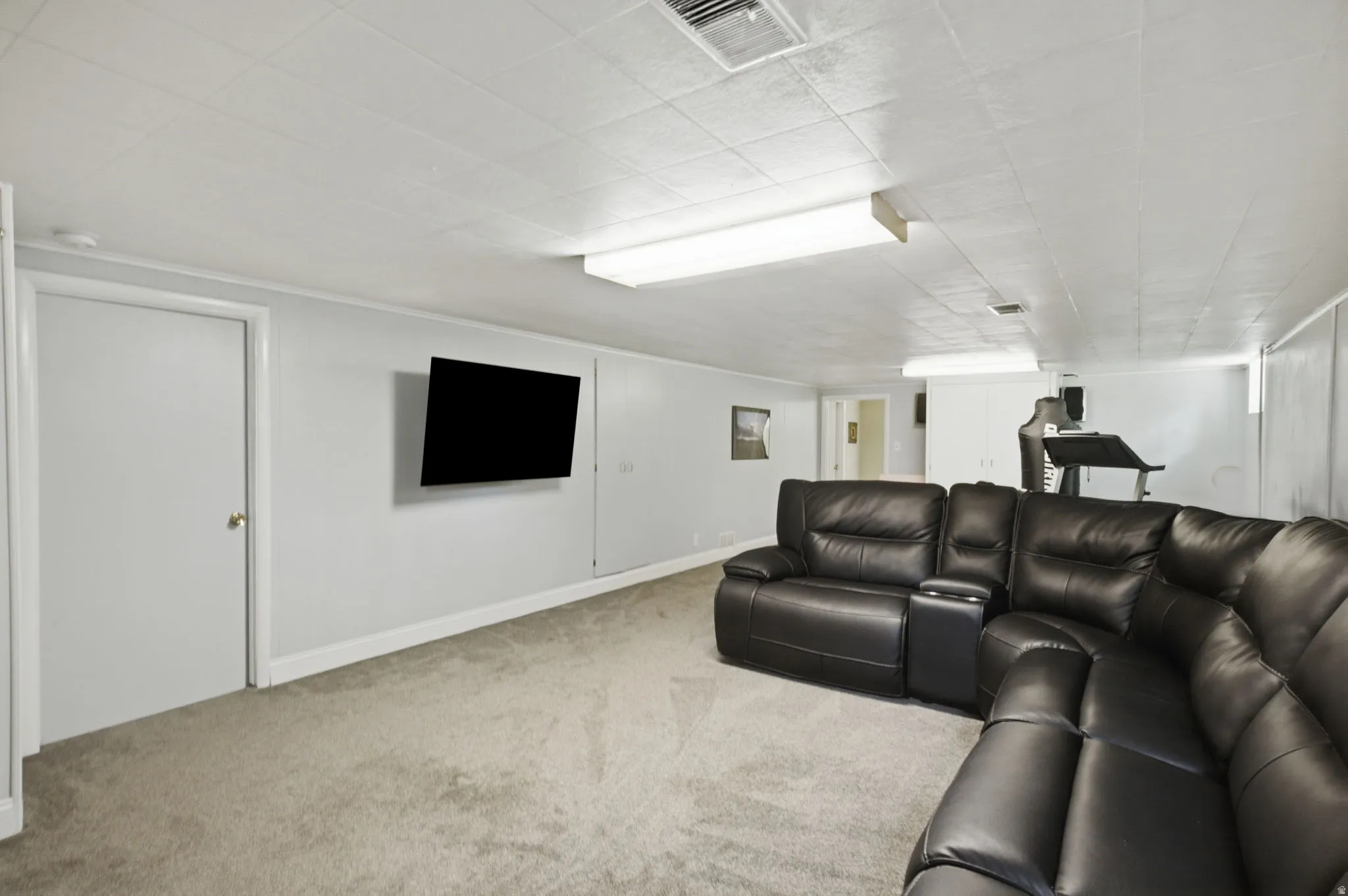 Carpeted recreation room featuring light gray walls, white baseboards, and a white ceiling with recessed lighting panels