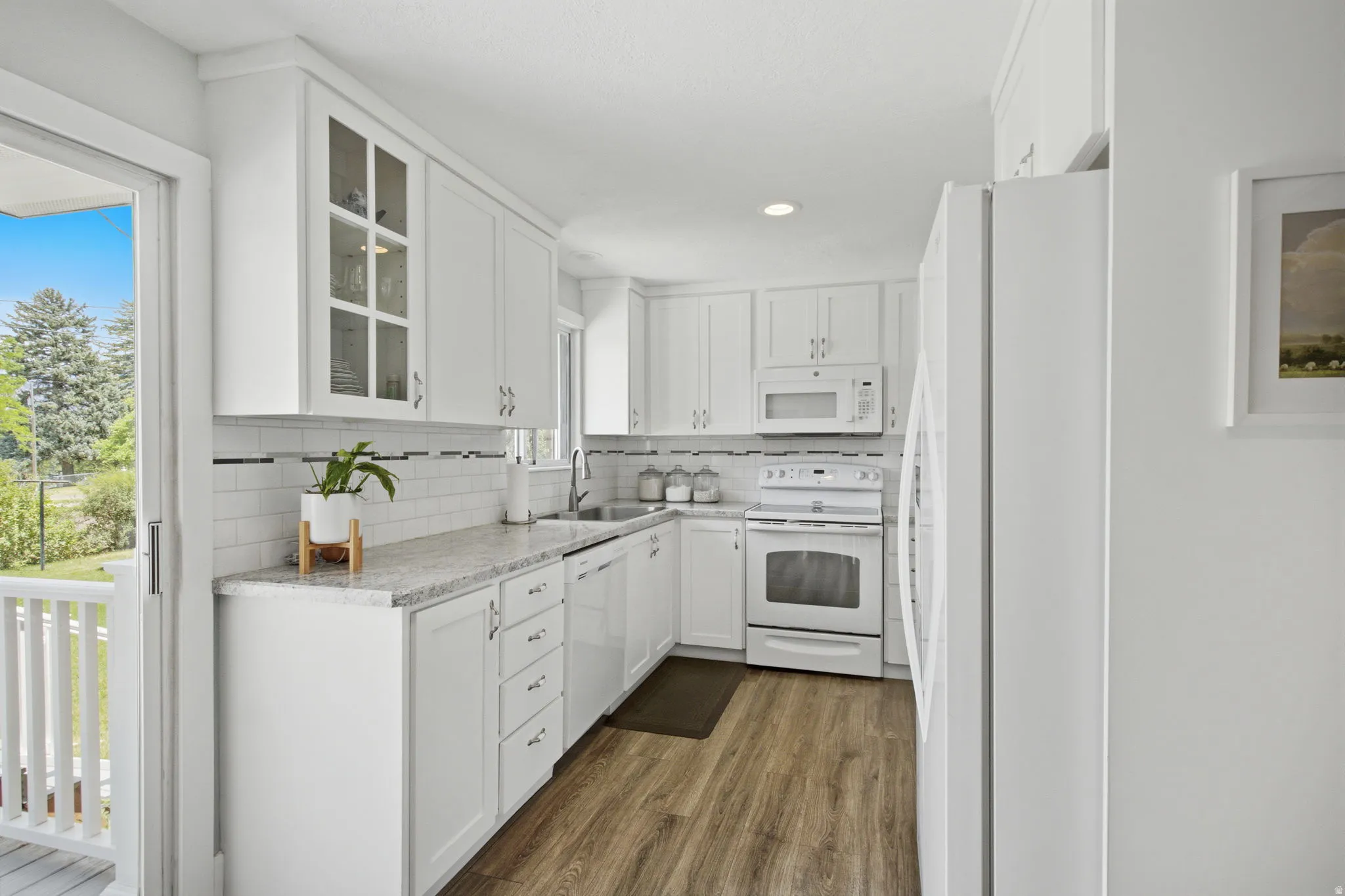Kitchen featuring white cabinetry, light-toned countertops, subway tile backsplash, wood-finish flooring, and a sliding glass door leading to an outdoor deck