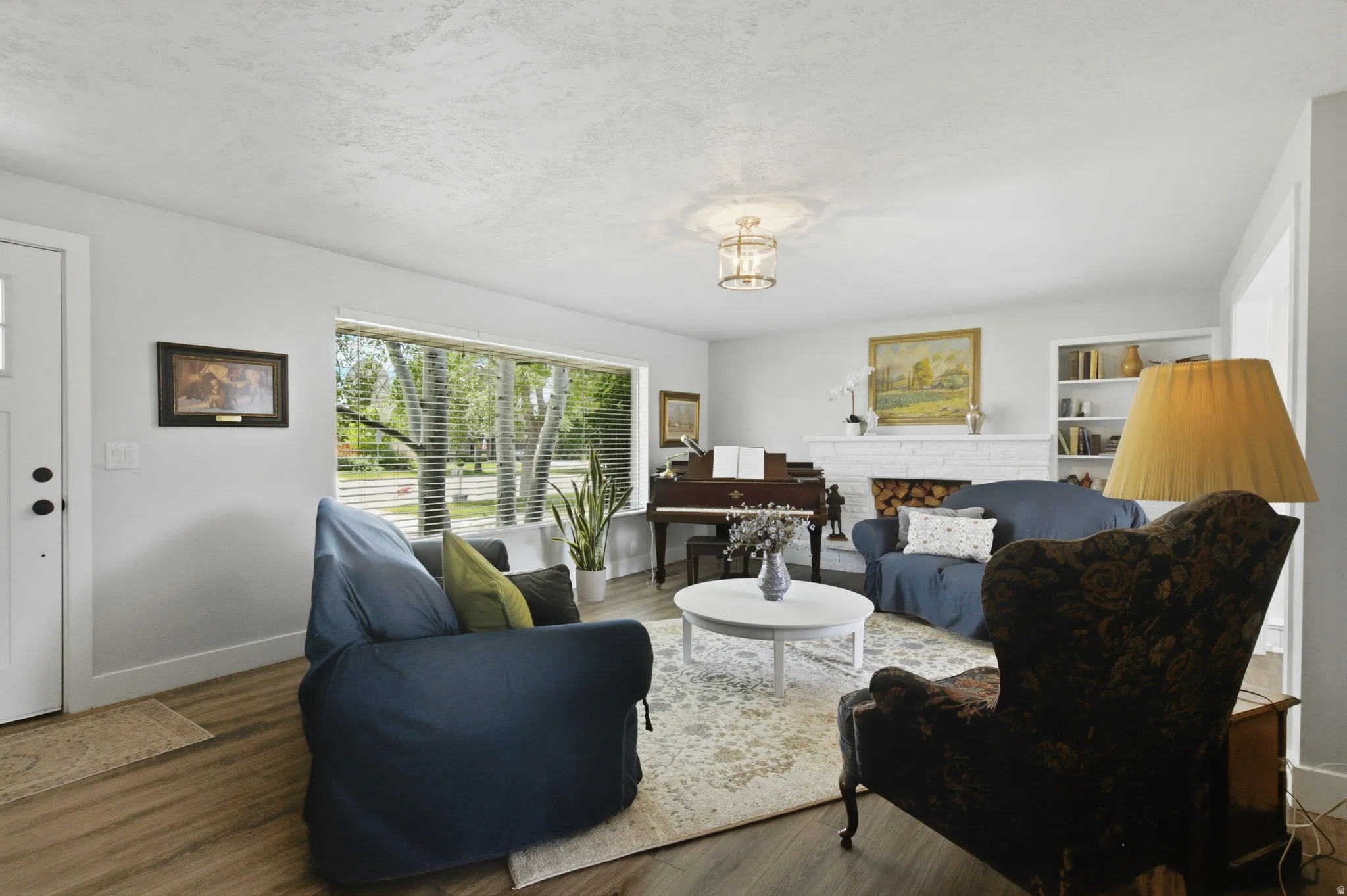 Expansive living area featuring wood-finish flooring, a white brick fireplace, and built-in shelving