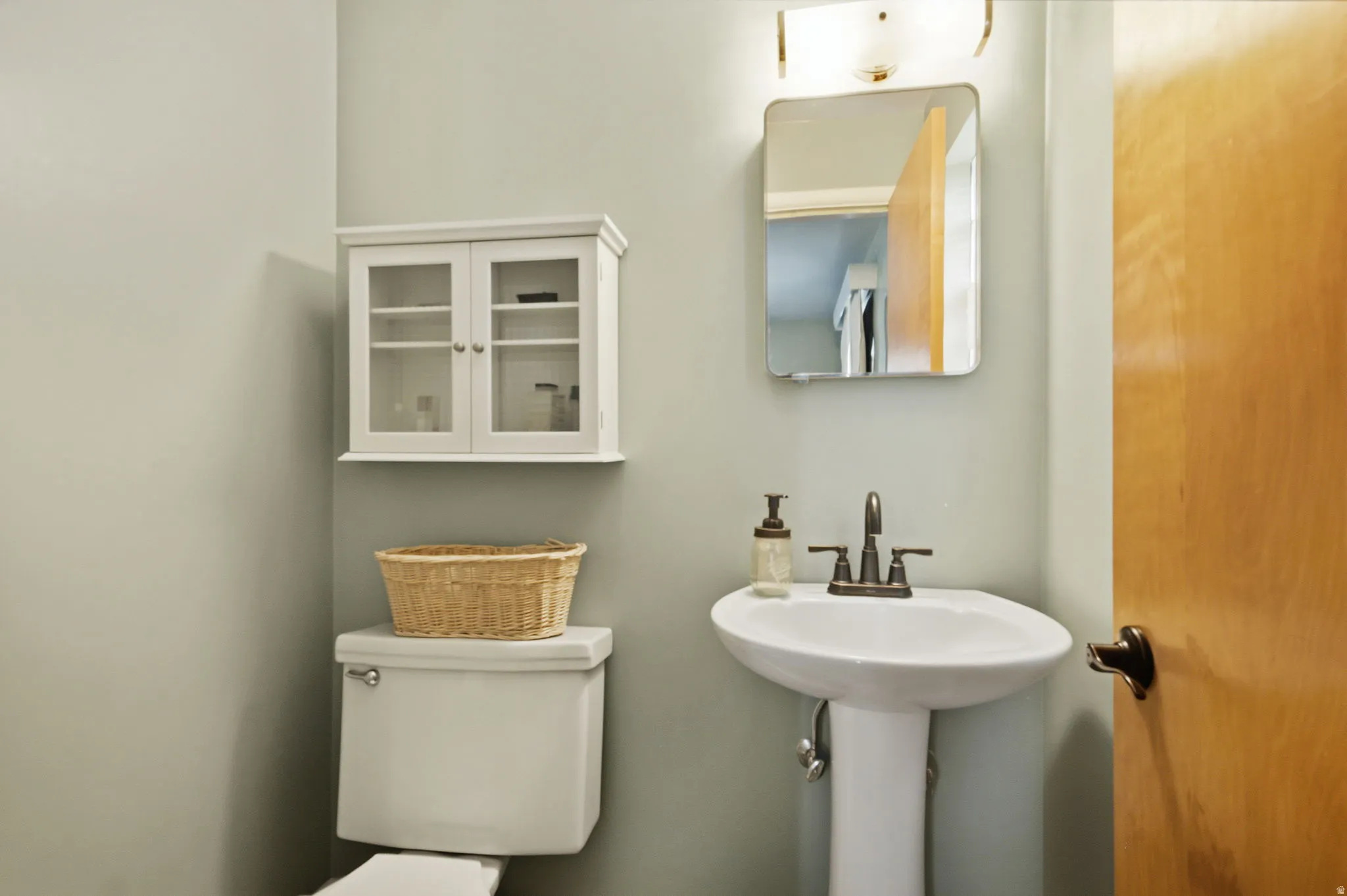 Pedestal sink with bronze-finish faucet, rectangular wall mirror, and modern vanity light fixture