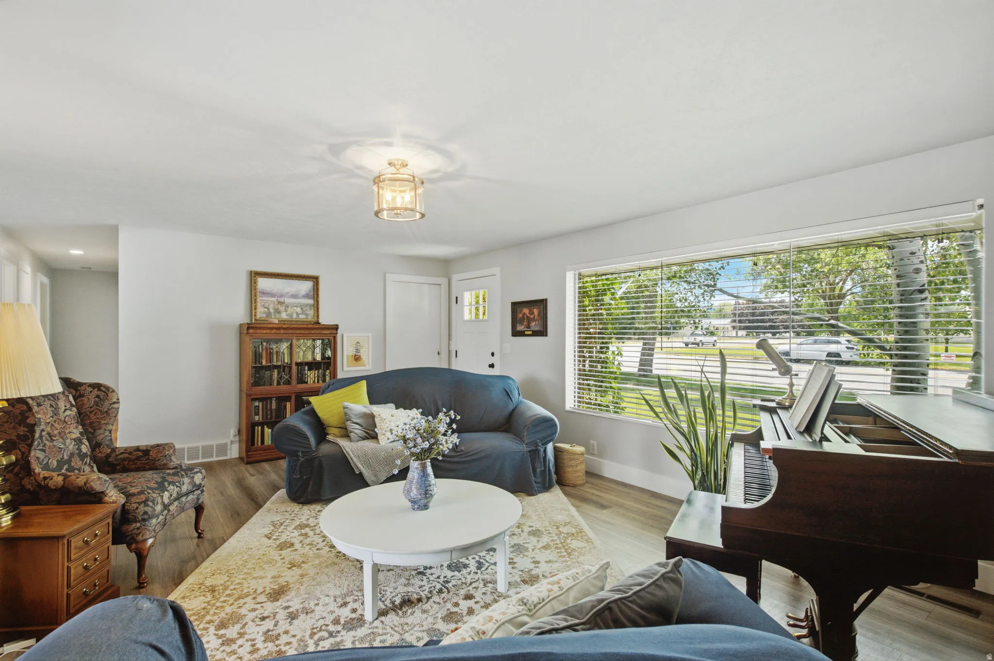 Spacious living area featuring light wood-finish flooring, a large picture window with blinds, and a built-in bookshelf
