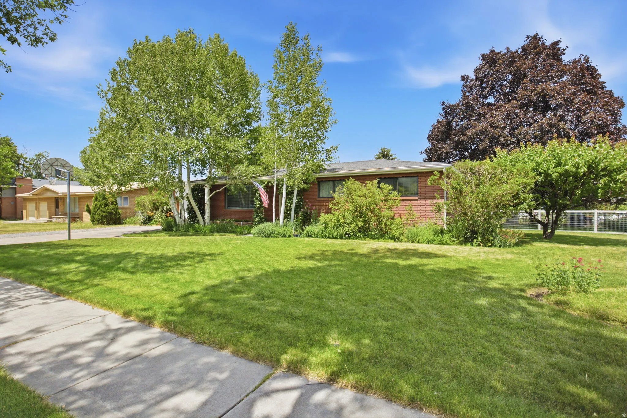 Brick exterior residence featuring a front lawn, mature trees, and established shrubbery