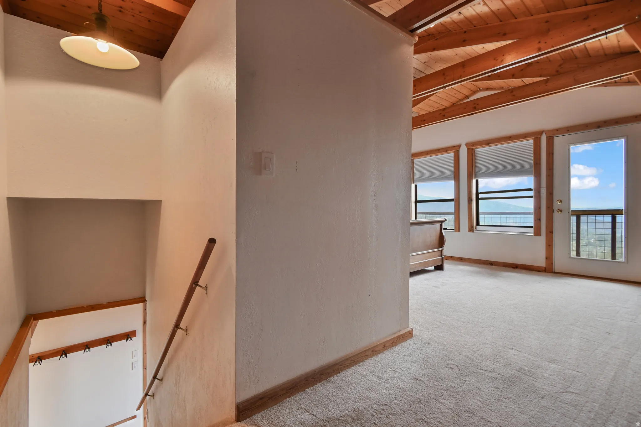 Carpeted room with exposed wood beam ceiling, wood-trimmed windows, and a glass-paneled door