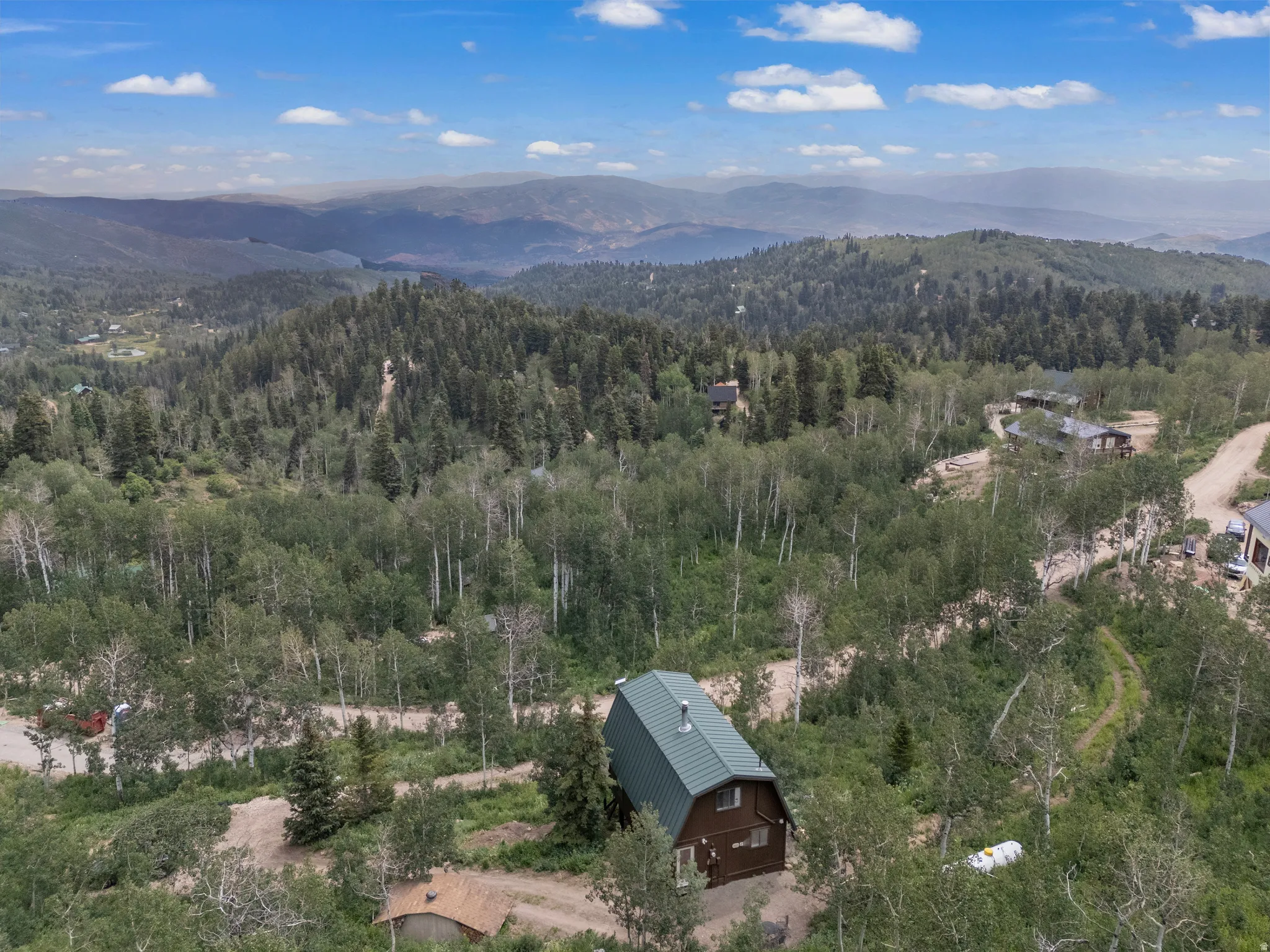 Rustic mountain cabin with a green metal roof and brown siding, surrounded by mature trees