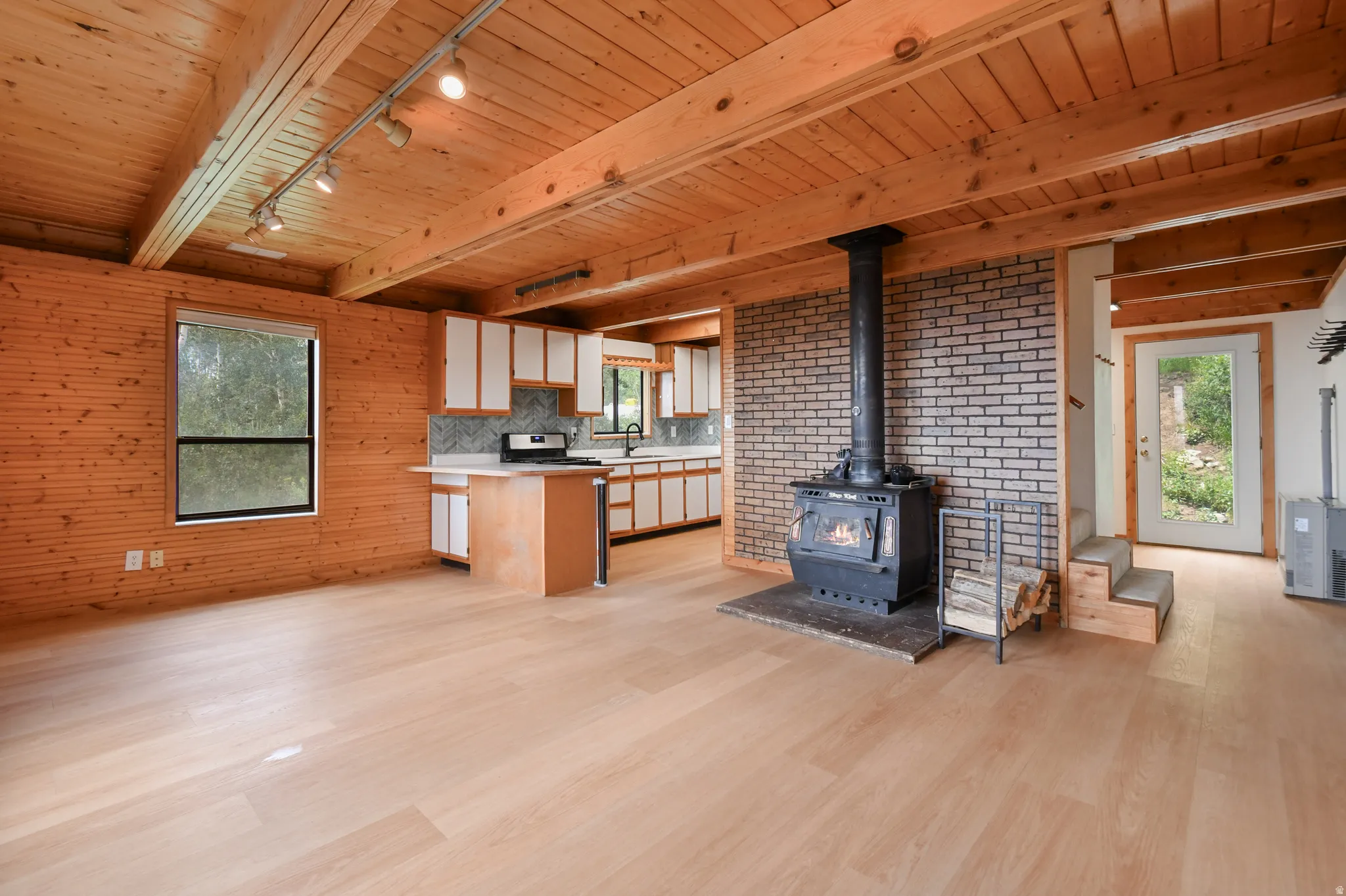 Open-concept living space featuring wood-finish flooring, exposed wood beam ceiling, and horizontal wood paneling
