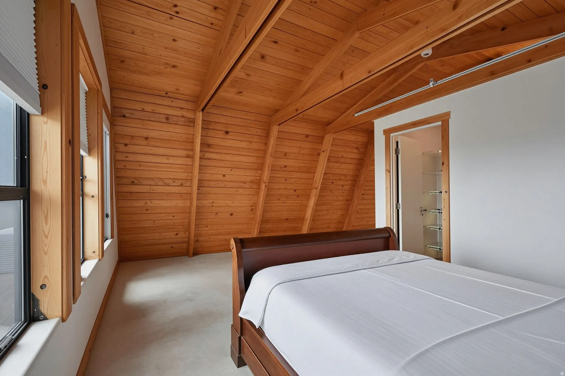 Vaulted wood-paneled ceiling with exposed beams, wood-frame windows, light-colored flooring, and a doorway revealing built-in shelving
