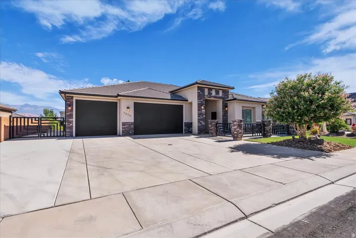 Contemporary stucco exterior with stone accents, featuring a two-car garage with dark doors and an expansive concrete driveway
