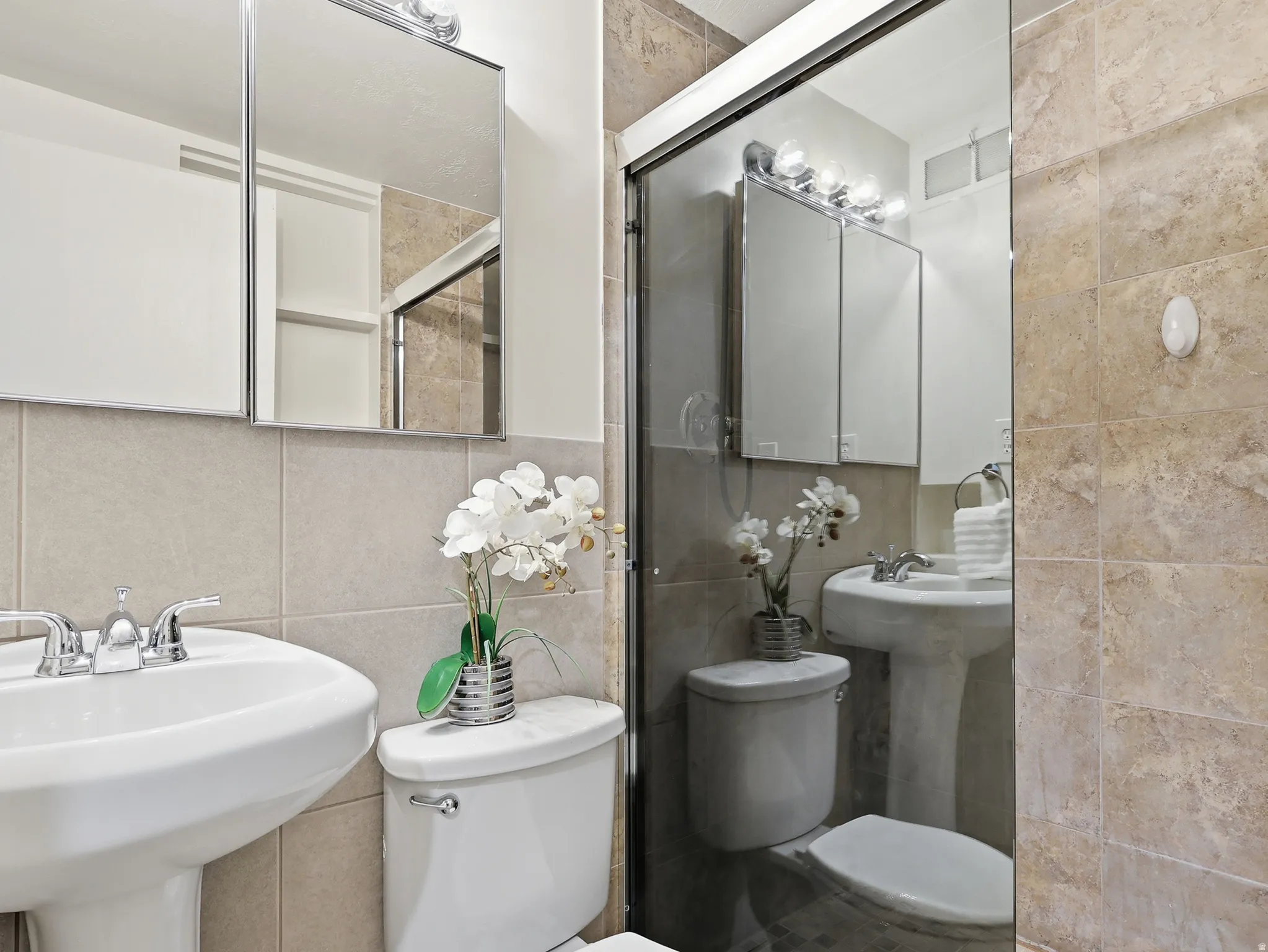 Bathroom with a pedestal sink, white toilet, and tile walls