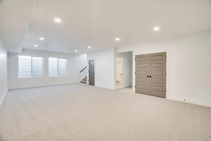 Spacious room featuring light-colored carpeting, multiple recessed ceiling lights, and three visible egress windows with blinds