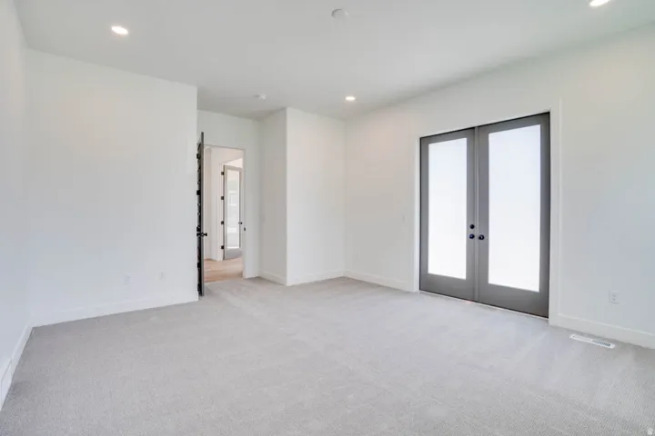 Interior room featuring light gray carpeting, white walls, recessed ceiling lighting, and a pair of gray French doors with opaque glass panels