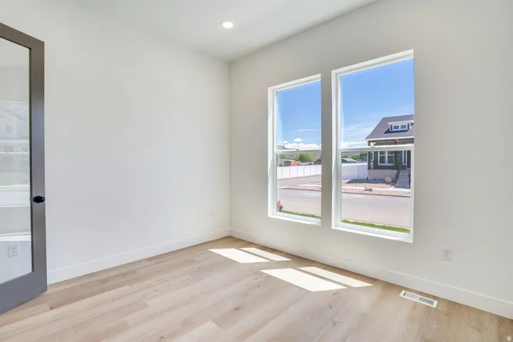 Bright interior space featuring two tall windows, wood-finish flooring, white baseboards, and a dark-framed glass panel door