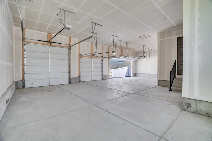 Spacious multi-car garage featuring concrete flooring, multiple overhead garage doors, exposed wall studs, and overhead storage racking