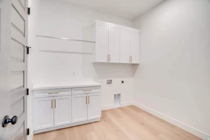 Utility room featuring white cabinetry, a light-toned wood-finish floor, a laundry hookup area, a white countertop, and a clothes hanging rod