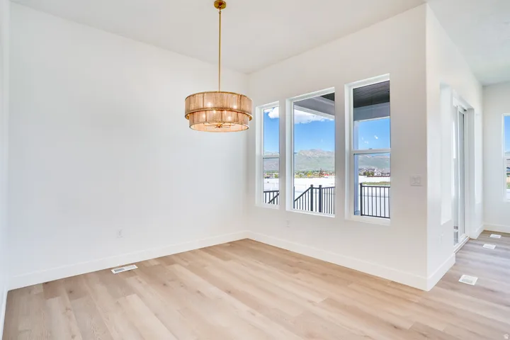 Spacious room with light wood-finish flooring, a contemporary tiered chandelier, white walls, and multiple windows offering mountain and water scenery
