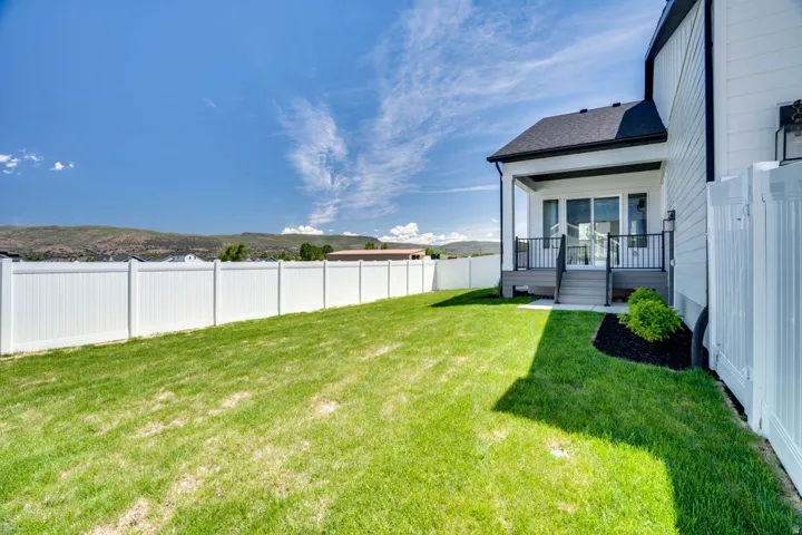 Expansive backyard featuring a manicured lawn, a white vinyl privacy fence, and a covered patio with black metal railings