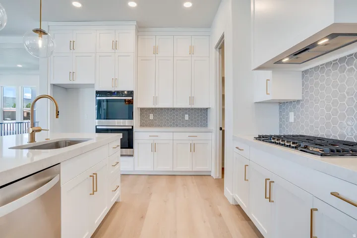 Contemporary kitchen featuring white cabinetry, light wood-finish flooring, a stainless steel sink with a gold-tone faucet, integrated wall oven, and a gas cooktop with a honeycomb tile backsplash