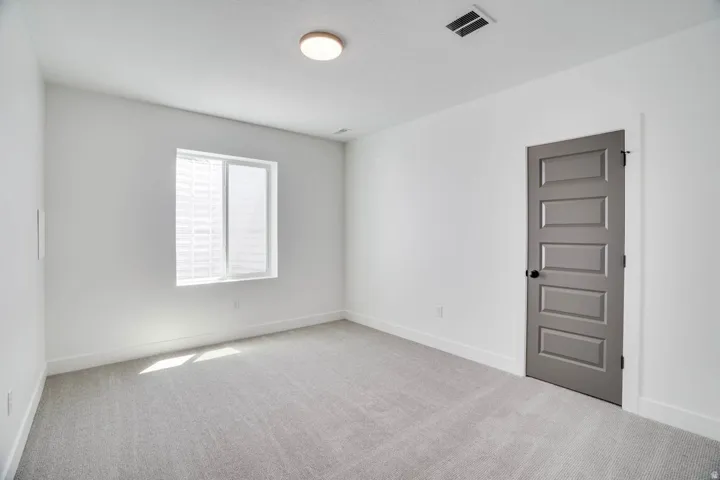 Bright interior space featuring a window with white blinds, light gray carpet, white walls, and a five-panel interior door with a matte black knob