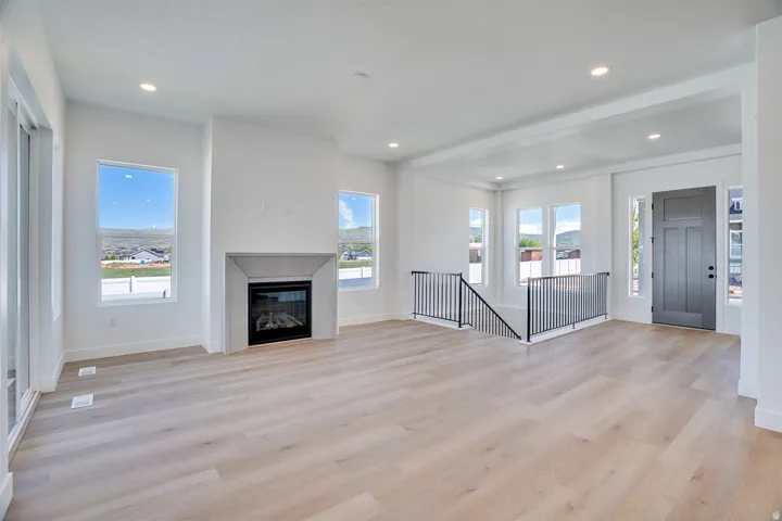 Spacious living area featuring light wood-finish flooring, a contemporary fireplace with a stone surround, recessed lighting, and large windows